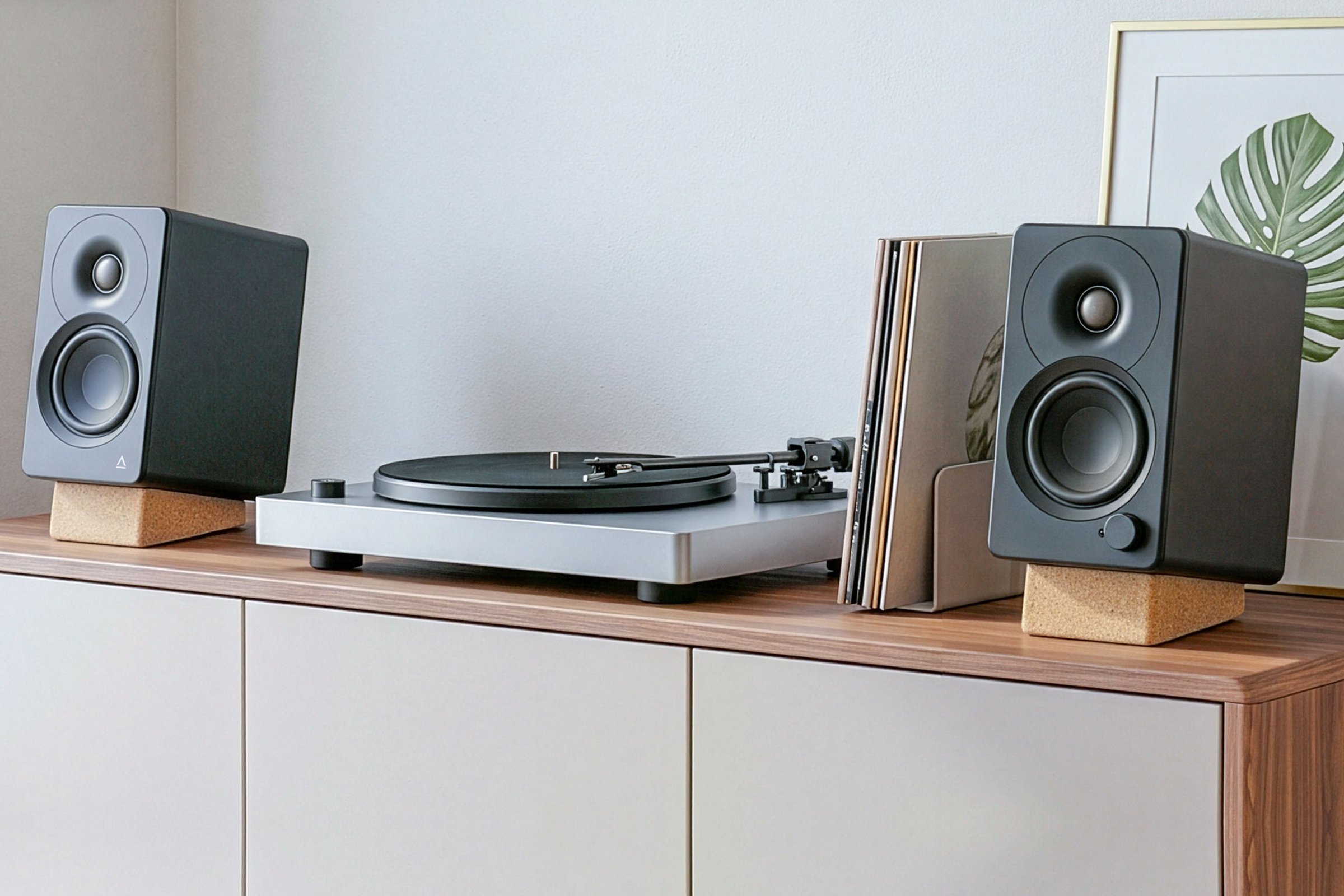 A pair of black Creative XF1 speakers on cork stands either side of a turntable on a timber sideboard