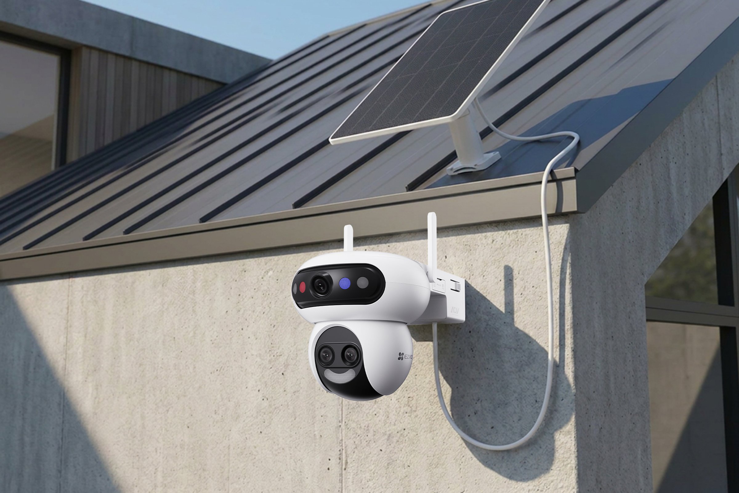 An EZVIZ HB90f camera with two lens units mounted on a concrete wall under a metal roof, wired to a small solar panel on the roof