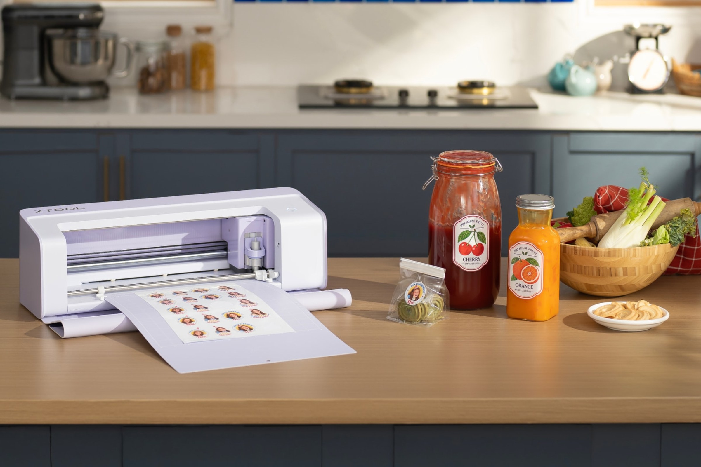 An xTool C1 Color Cutter on a kitchen bench with a sheet of printed stickers, beside two jars wearing cherry and orange labels